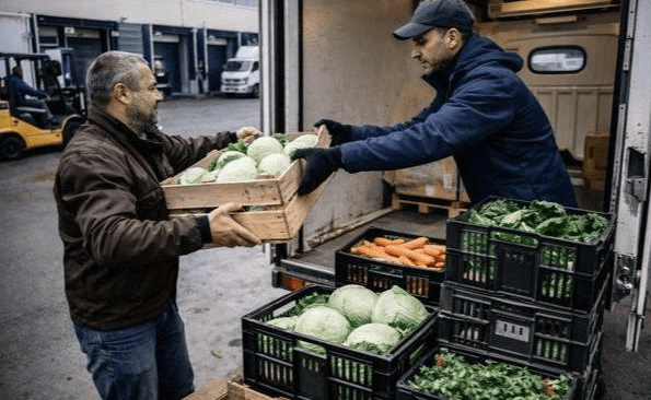 Deux personnes déchargeant des cageots de légumes d'un camion